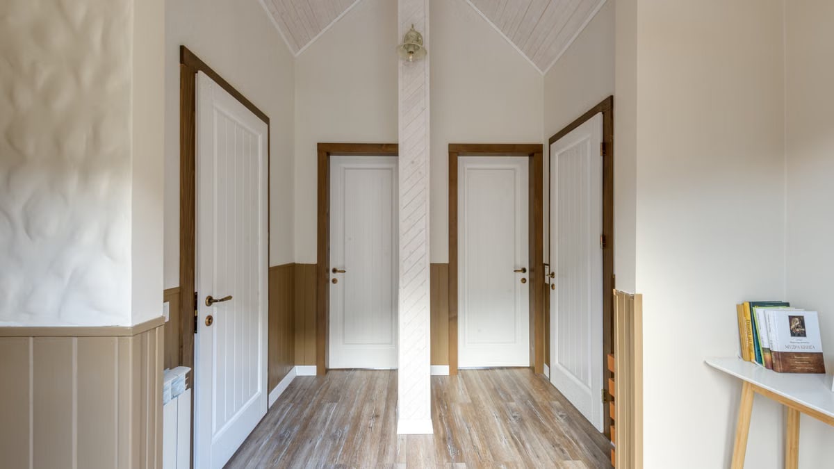 Bright hallway with wooden flooring and three doors, offering a cozy homey feel.